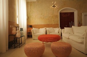 Un salon avec un ensemble de canapés blancs, un pouf rouge et une petite table sur laquelle sont posées des bougies.