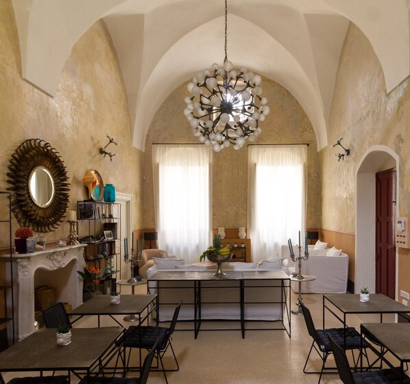 A dining area with a high arched ceiling, a chandelier, and a view of the kitchen through the windows. - Casa Galateo 20 (Gallipoli)