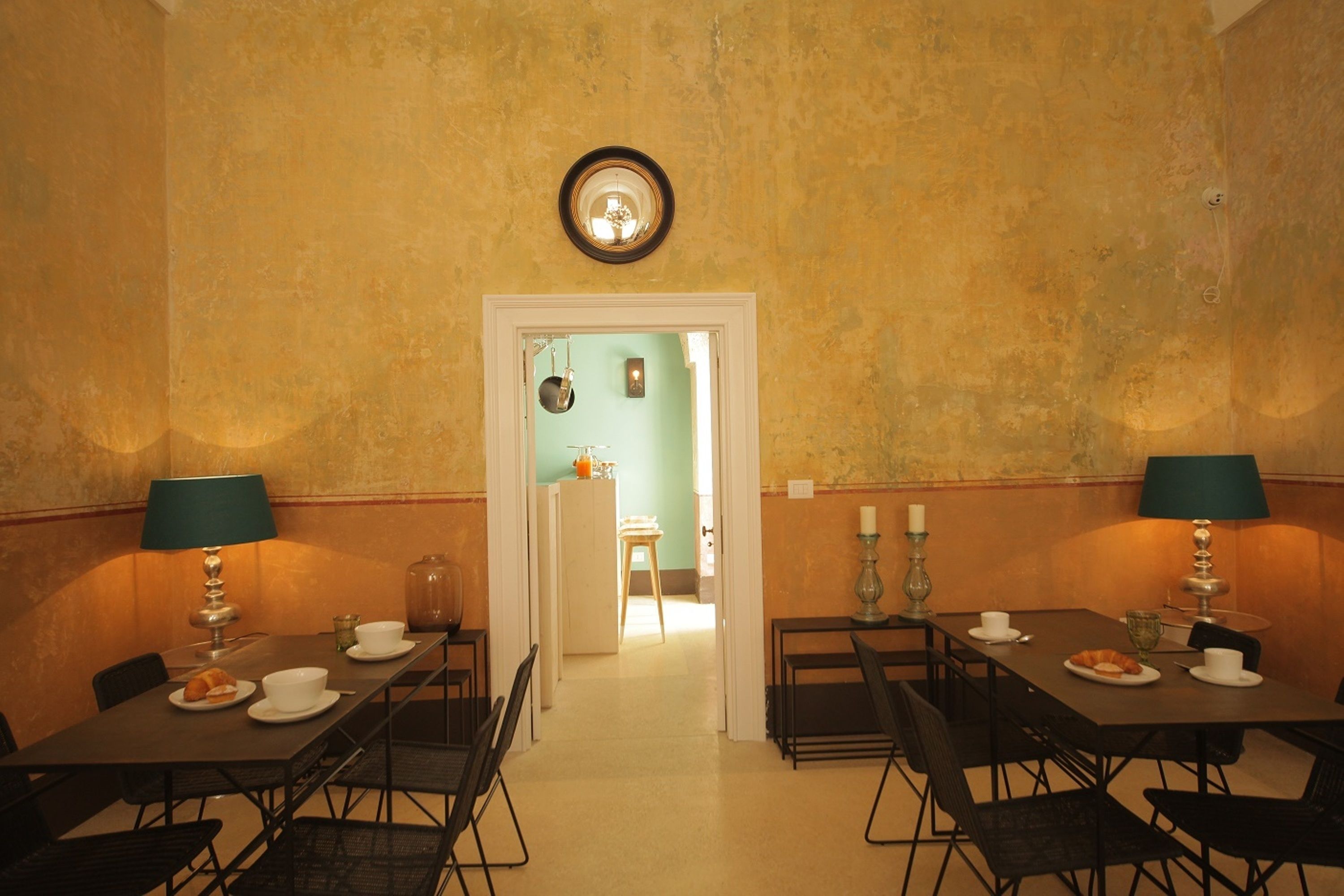 Un comedor con mesas y sillas, un espejo en la pared y una puerta que da a otra habitación.