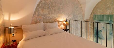 A bedroom with a large bed, a nightstand with a lamp, and a view of a balcony.
