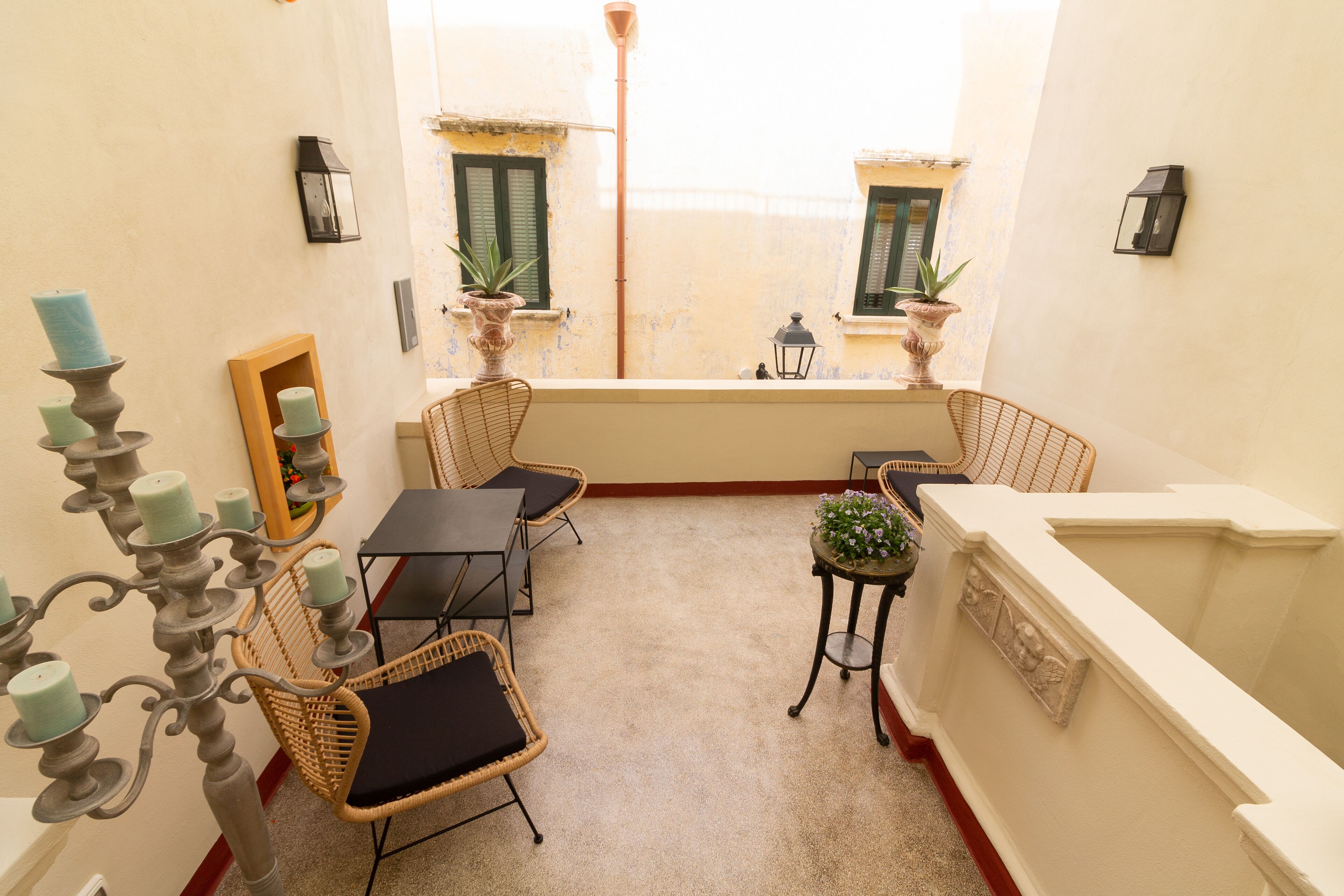 A narrow balcony with wicker furniture, a candelabra, and potted plants.
