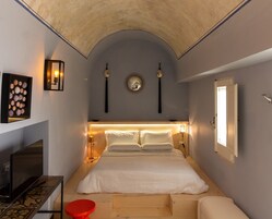 Une chambre à coucher avec un lit, des lampes de chevet, un miroir, un téléviseur fixé au mur et un petit tabouret rouge.