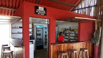 A bar area with a sign reading "AMBASSADE DE BRETAGNE AU TOGO". There are wooden stools and a refrigerator stocked with beverages.