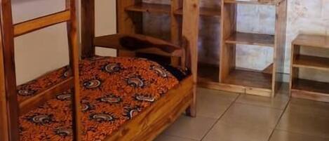 Habitación con literas, cabecera de madera, una mesita pequeña y colcha estampada.