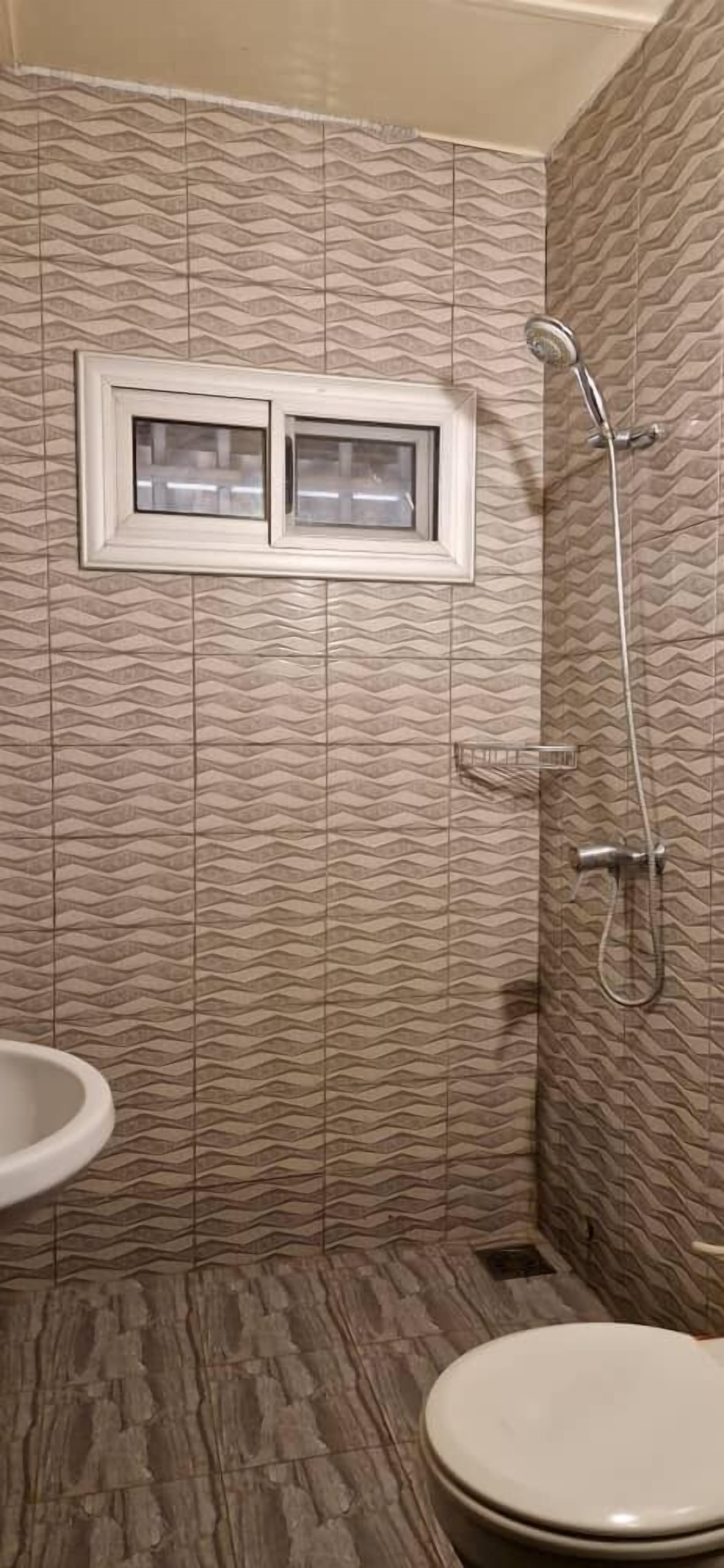 Un baño con baldosas estampadas, una ventana, una ducha y un inodoro.