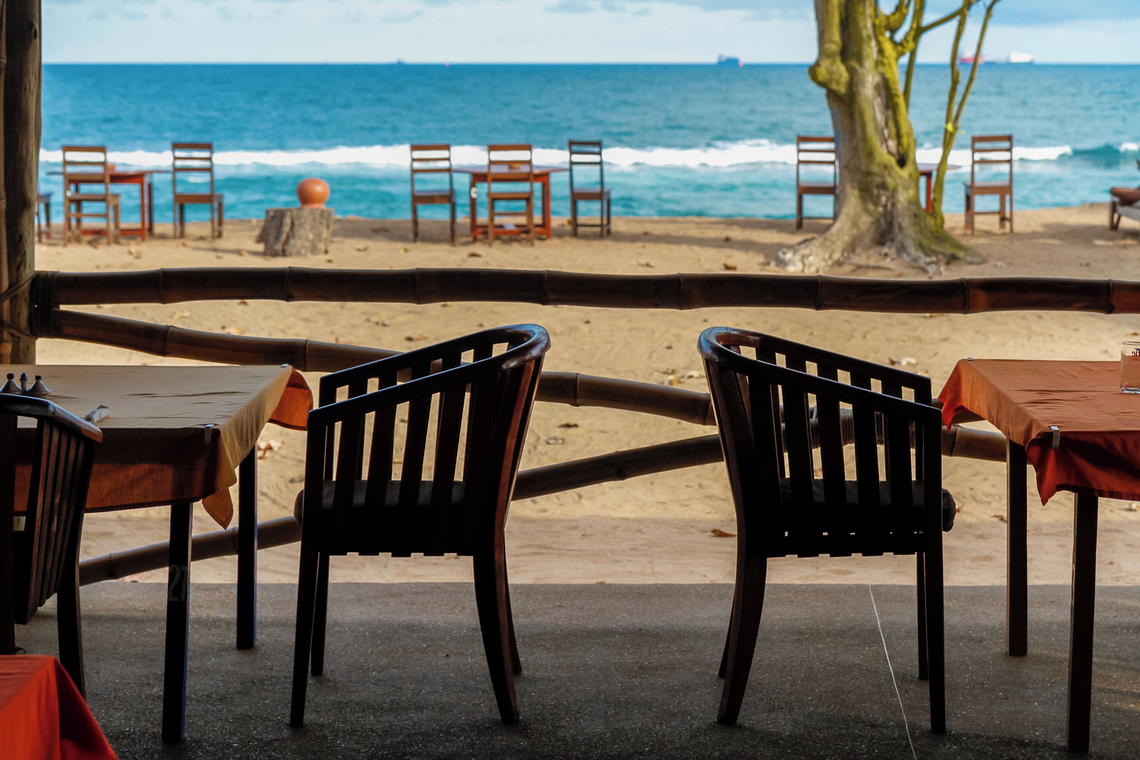 A beachside seating area with wooden tables and chairs, overlooking the ocean.