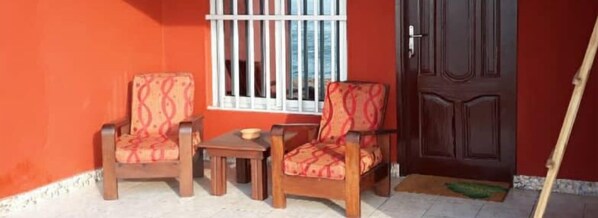 Una habitación con dos sillas de madera, una mesita y un ventanal con barrotes blancos.