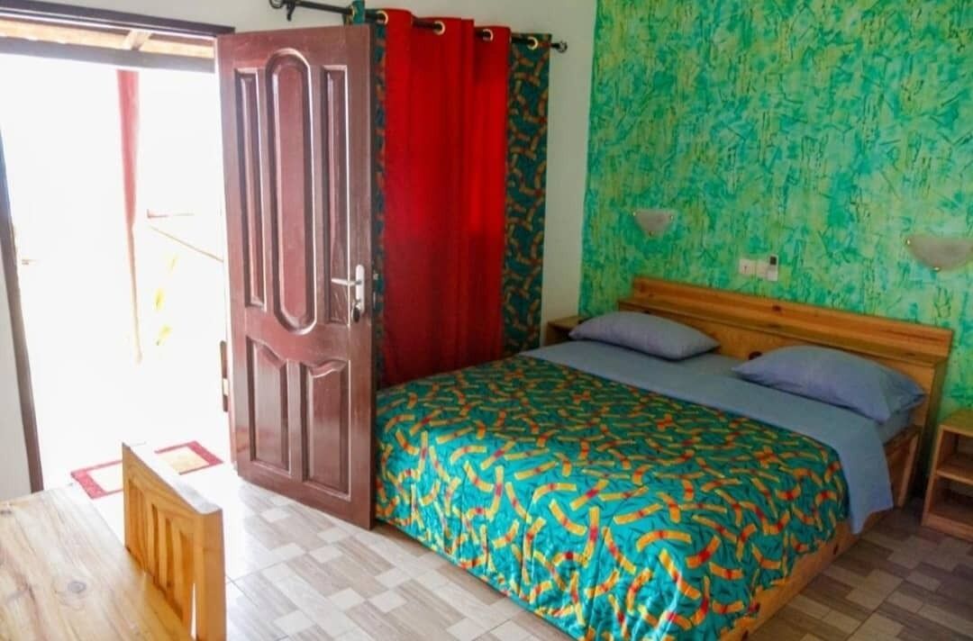 Ein Schlafzimmer mit einem Bett, einem hölzernen Kopfteil, einer roten Tür und einer Wand mit grünem Muster.