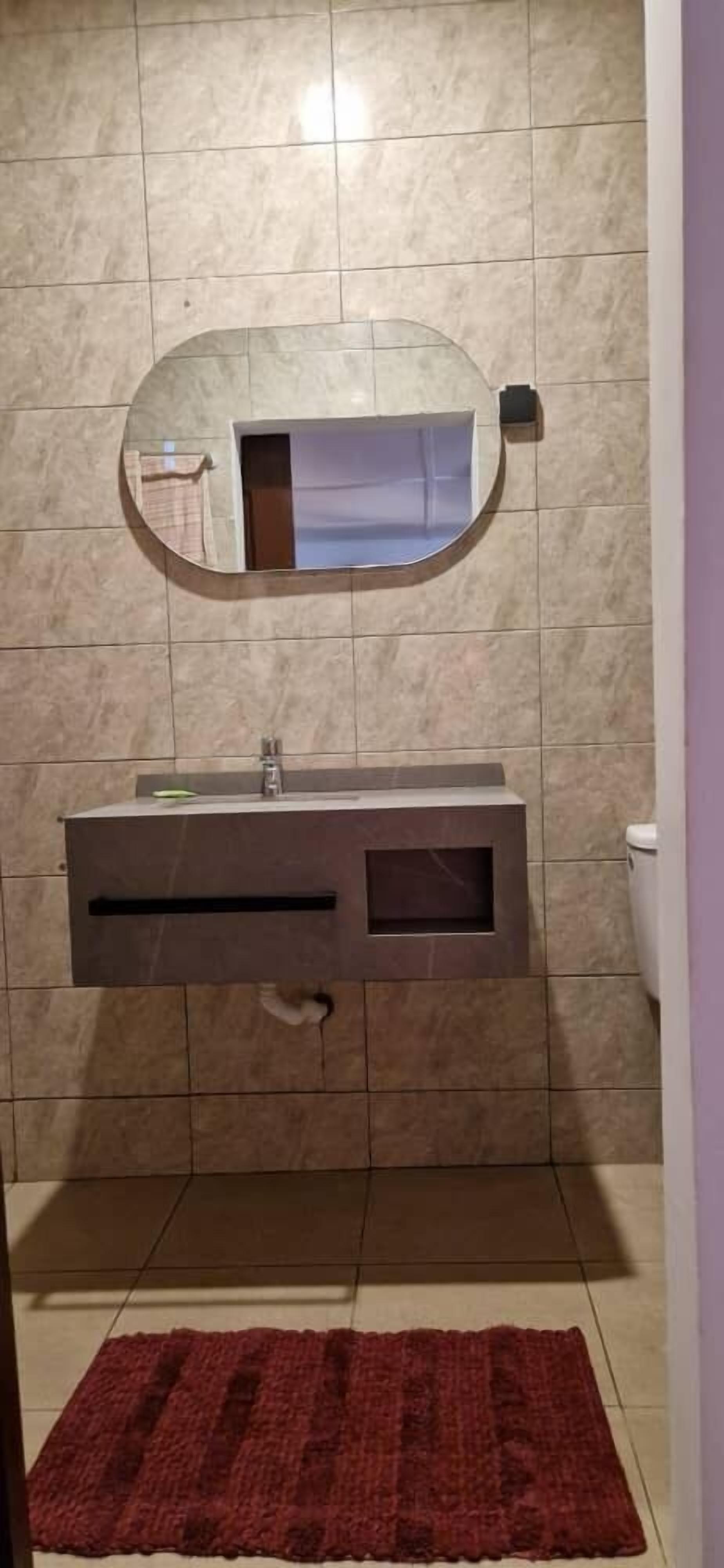 Un bany amb paret revestida de marbre, un mirall rodó, un lavabo integrat amb un armari i una catifa vermella al terra.
