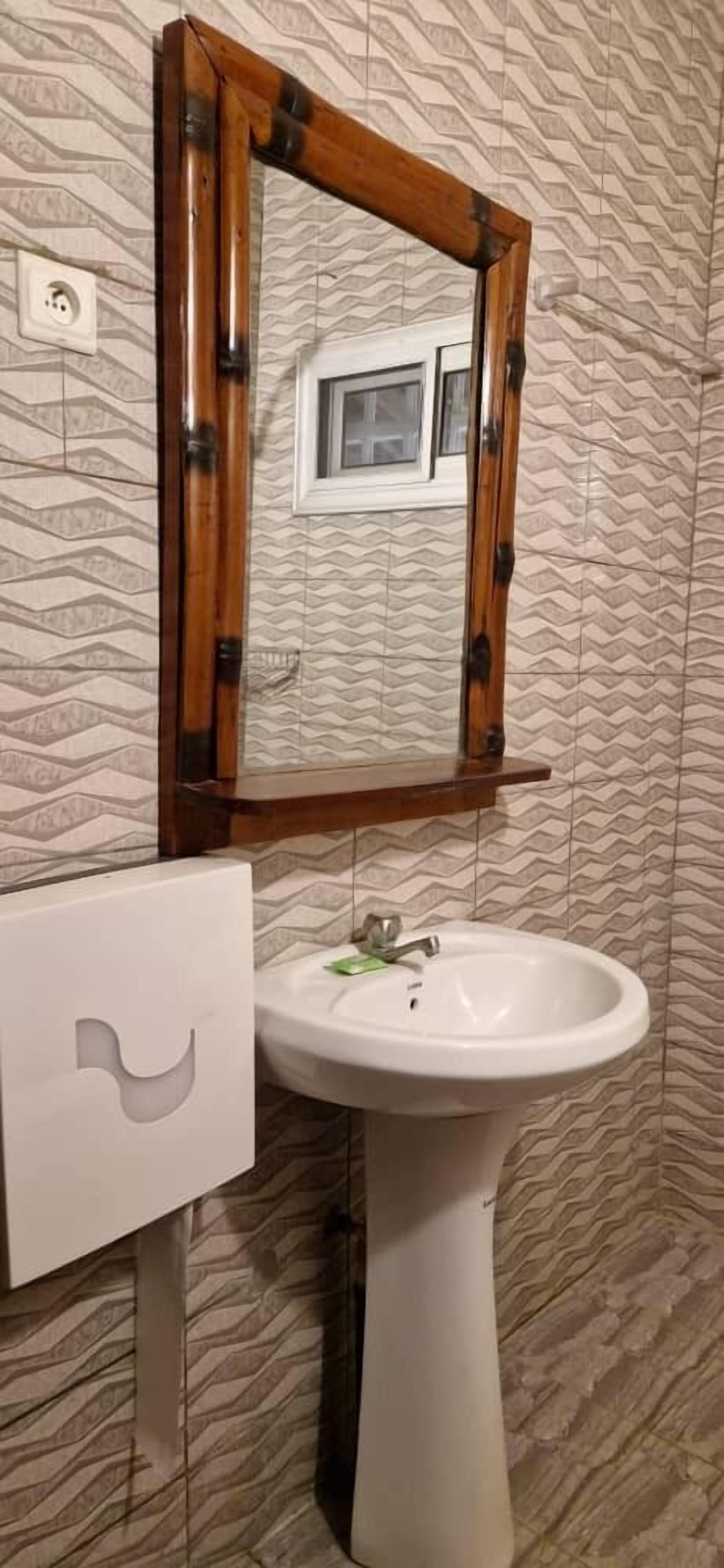 A bathroom with a white sink, a wooden-framed mirror, and patterned wallpaper.