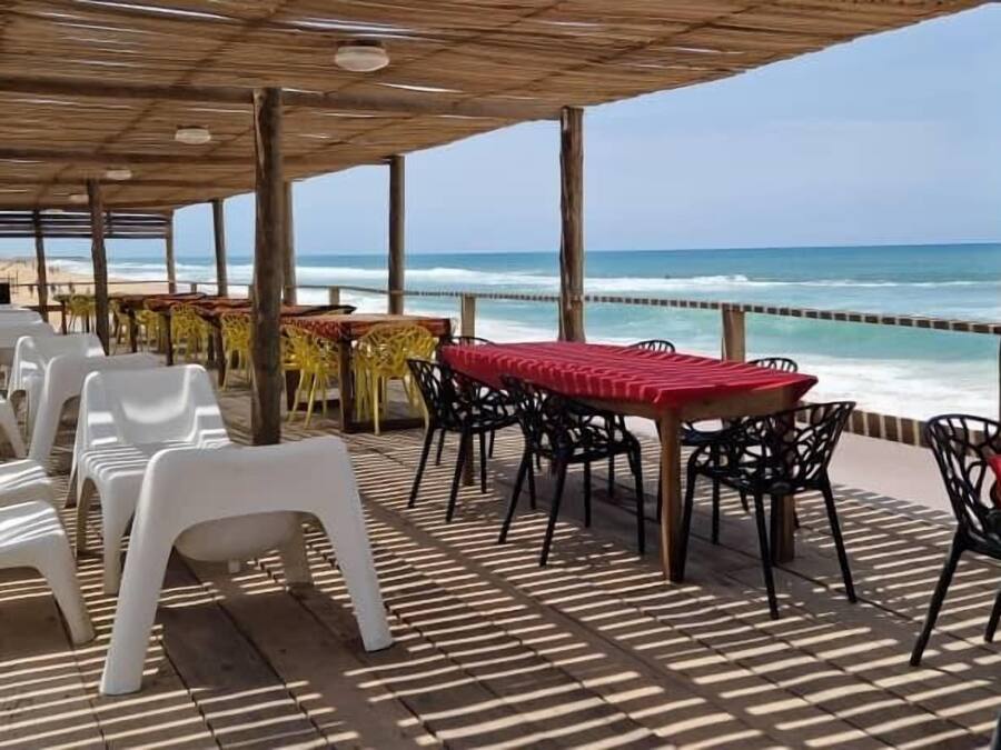 A beachside patio with plastic chairs and tables, a wooden deck, and a view of the ocean.
