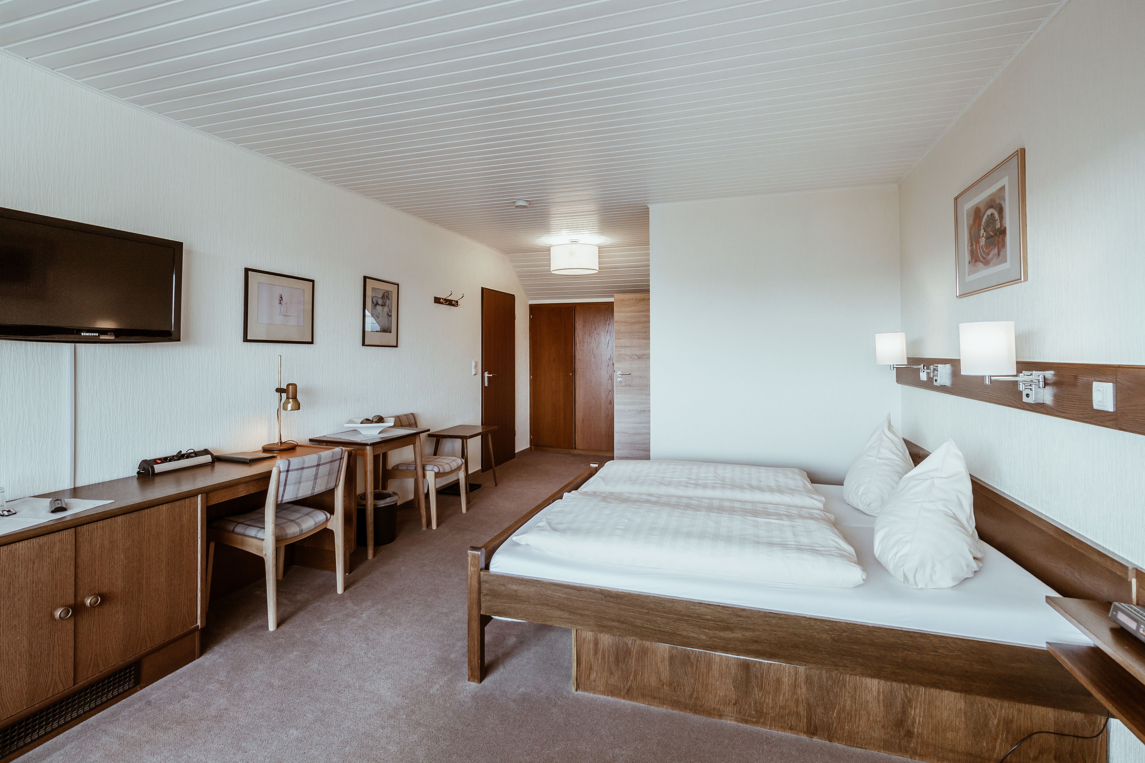 A hotel room with a bed, desk, chair, and a television.