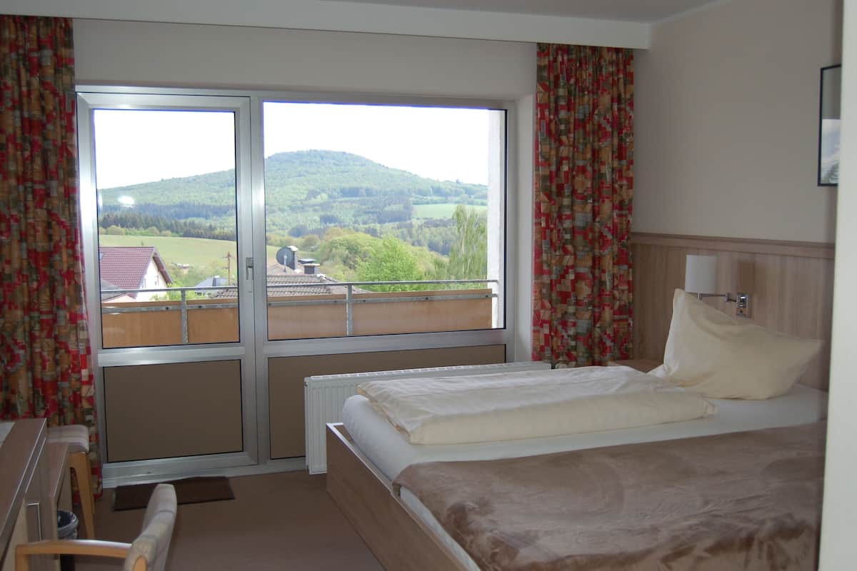 Ein Hotelzimmer mit Bett, einem Fenster mit Blick auf eine grüne Landschaft und Vorhängen.
