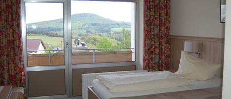 A hotel room with a bed, a window with a view of a green landscape, and curtains.