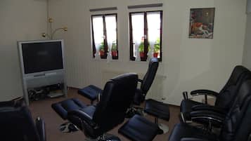 A living room with a flat-screen TV, black leather chairs, a radiator, and windows with curtains.
