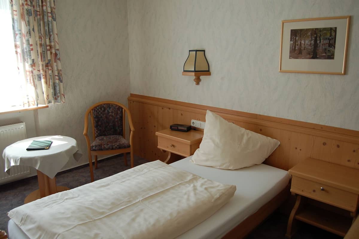 Ein Hotelzimmer mit Bett, Stuhl, Nachttisch, Tisch und Lampe.