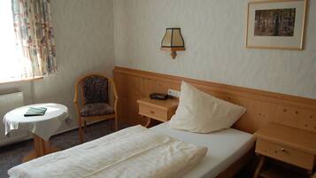 A hotel room with a bed, a chair, a nightstand, a table, and a lamp.