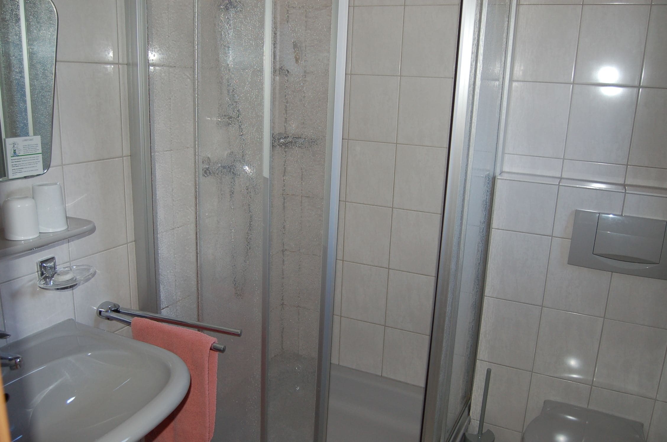 Un bagno con doccia vetrata, un lavandino con asciugamano rosa e uno specchio.