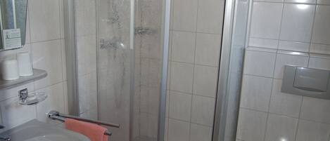 Un baño con ducha de mampara, lavamanos con una toalla rosa y un espejo.