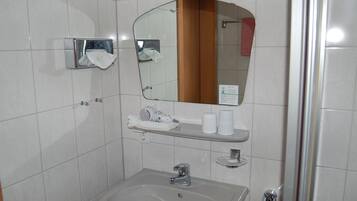 Un baño con lavamanos, espejo, dispensador de toallas y zona de ducha.