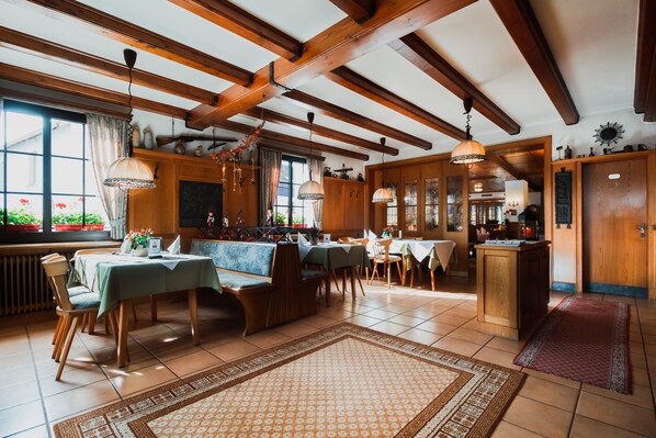 A spacious dining area with wooden beams, multiple tables, and chairs.