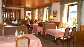A dining area with tables set for two, wooden chairs, and a buffet table with a roasted chicken centerpiece.