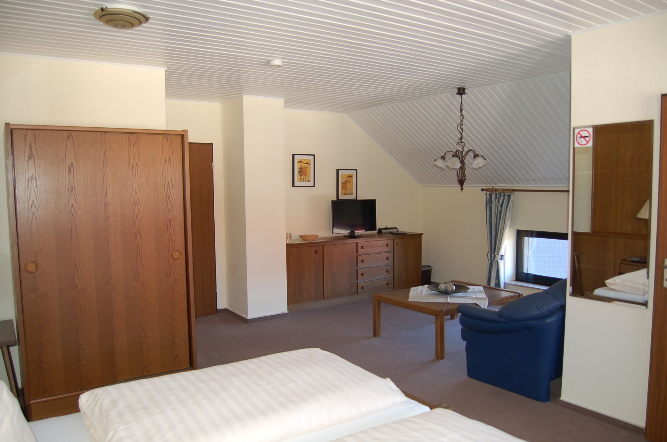 A hotel room with a bed, a desk, a chair, a television, and a wardrobe.