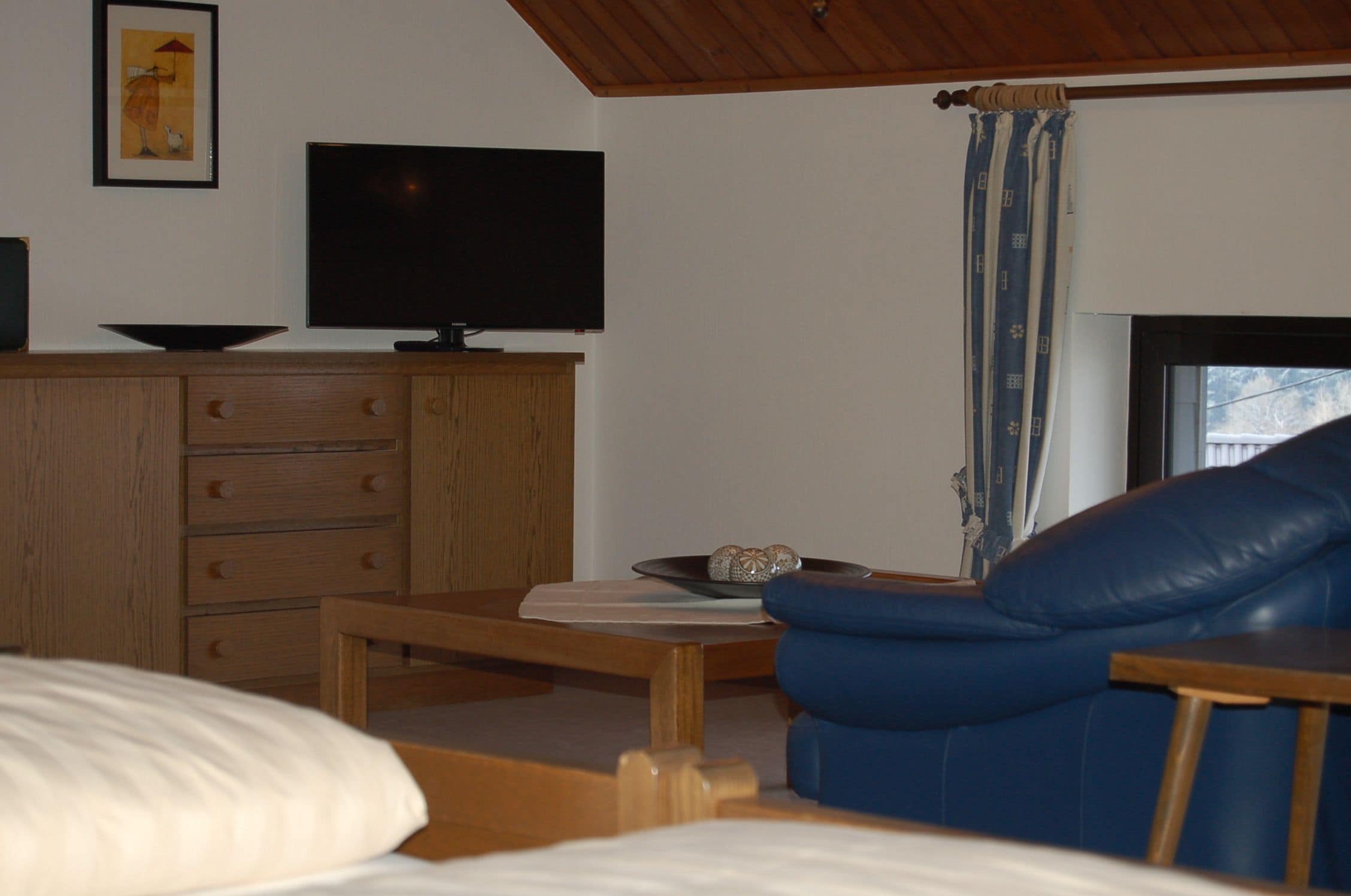 Una habitación con un armario de madera, televisión, un sofá azul y una ventana con cortinas.