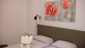 A bedroom with two beds, a painting of red flowers, a basket of towels, and a small shelf. - I Giardini di Elencosta (Misiliscemi)