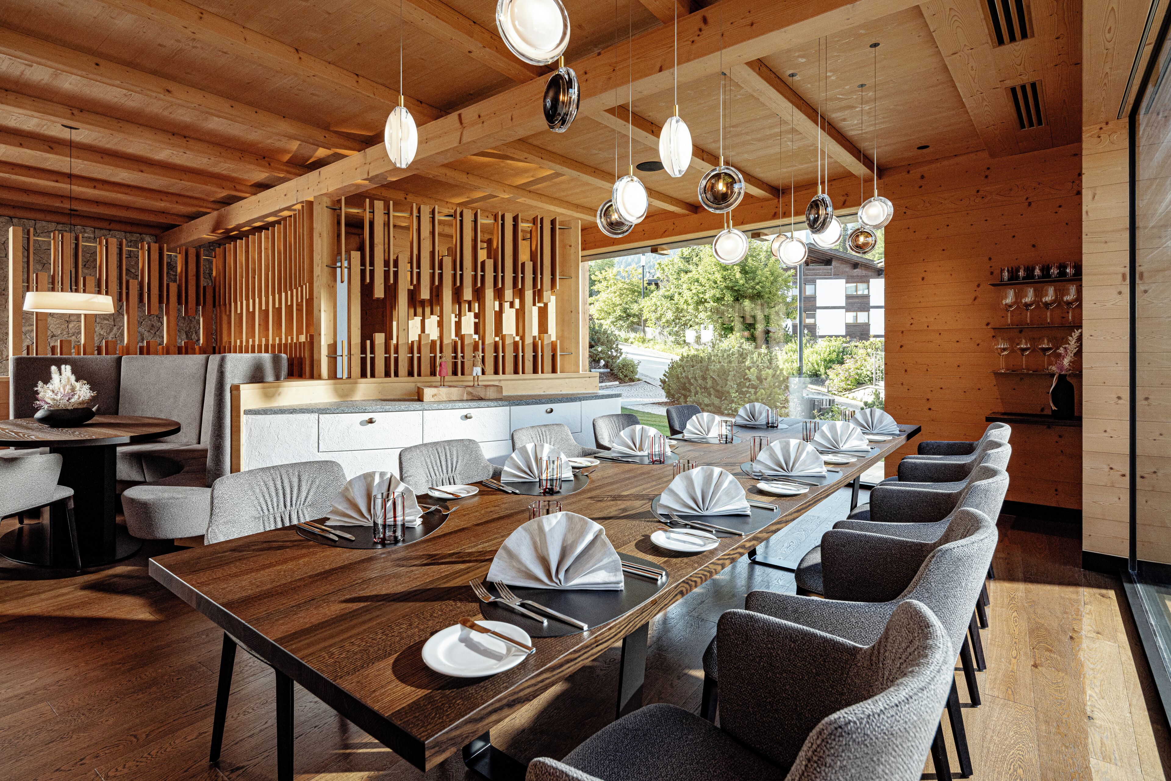 Un comedor moderno con una larga mesa de madera, sillas tapizadas en gris y lámparas colgantes.