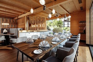 Un comedor moderno con una larga mesa de madera, sillas tapizadas en gris y lámparas colgantes.