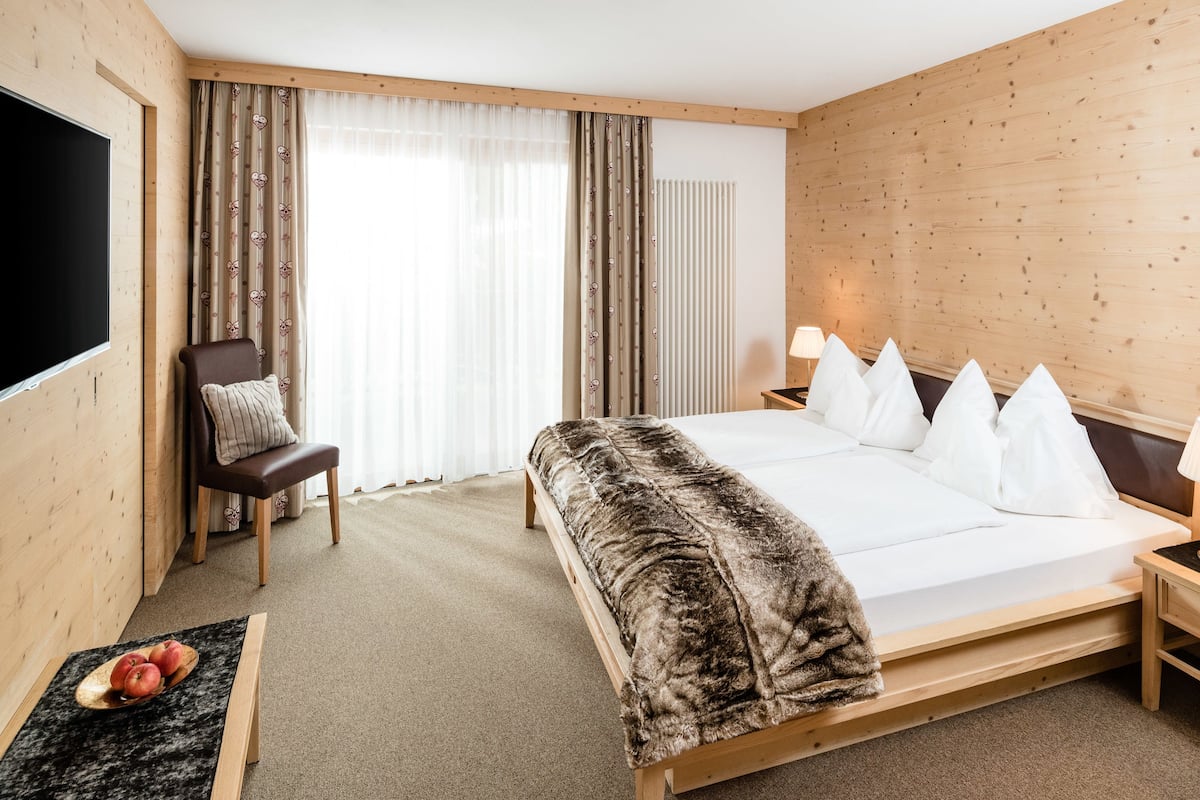 A hotel room with a large bed, a chair, a TV, and a bedside table with a lamp.