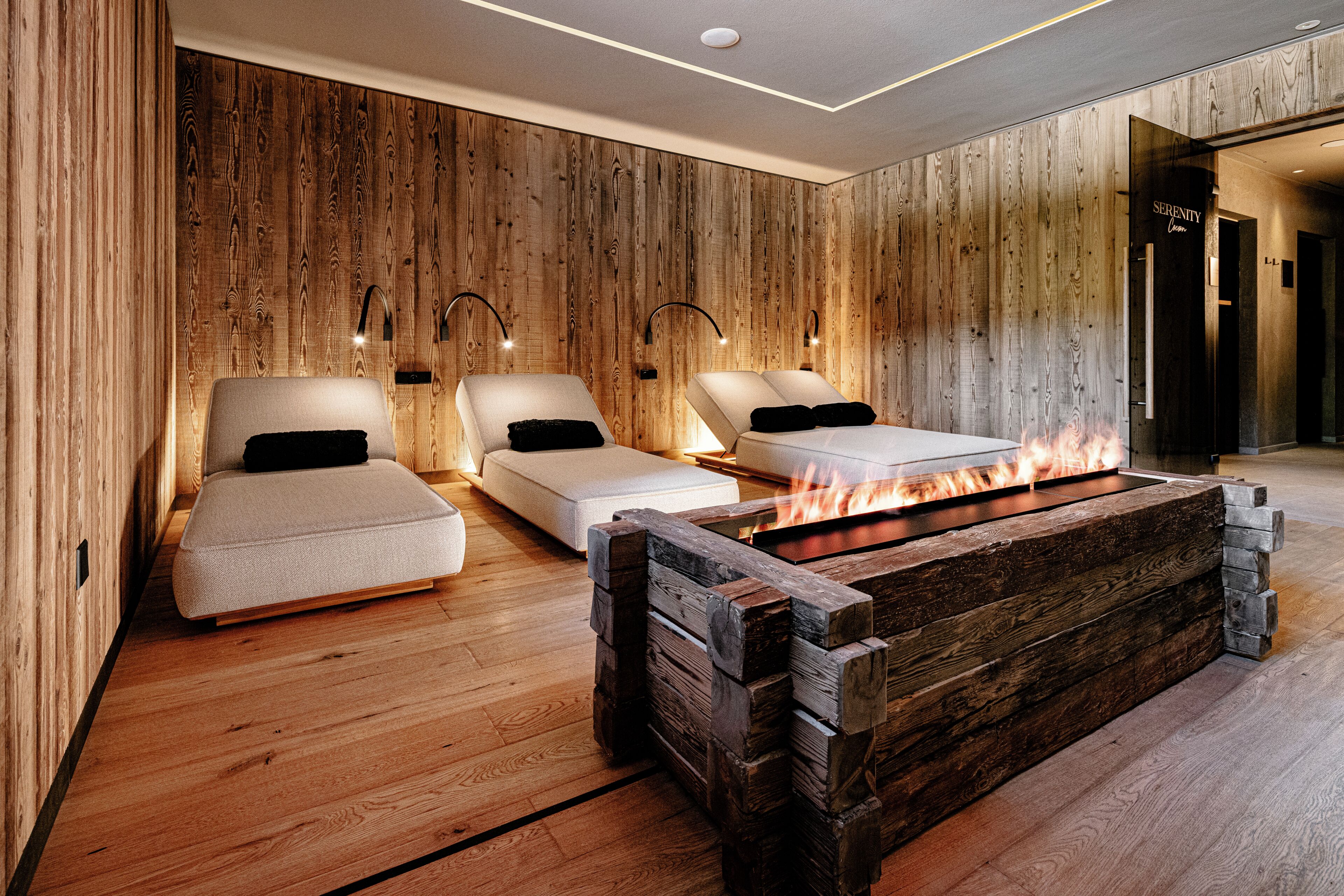 A modern room with wooden walls, two beds, a fireplace, and a reception area.