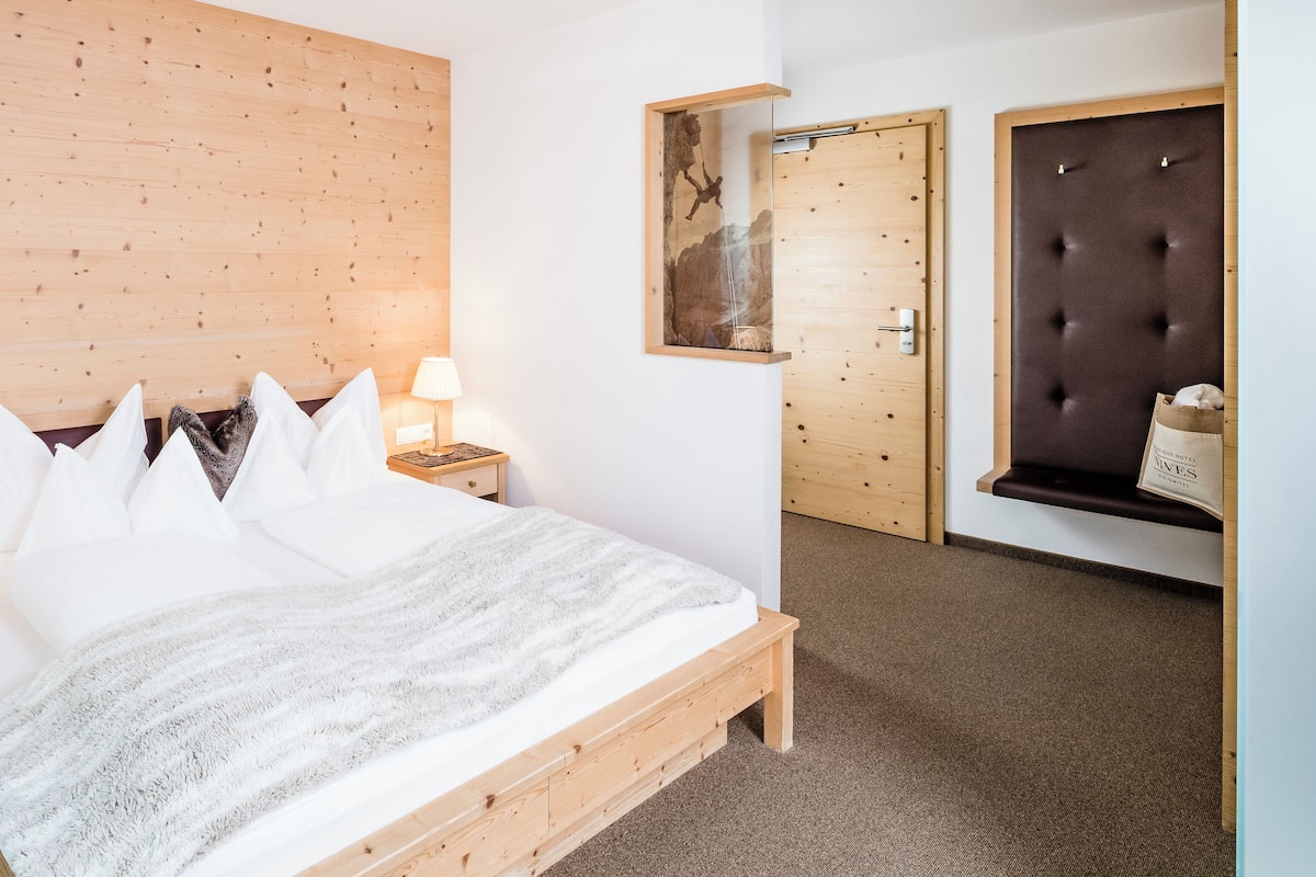 A wooden bed with white bedding, a nightstand with a lamp, a wooden headboard, and a door with a wooden panel.