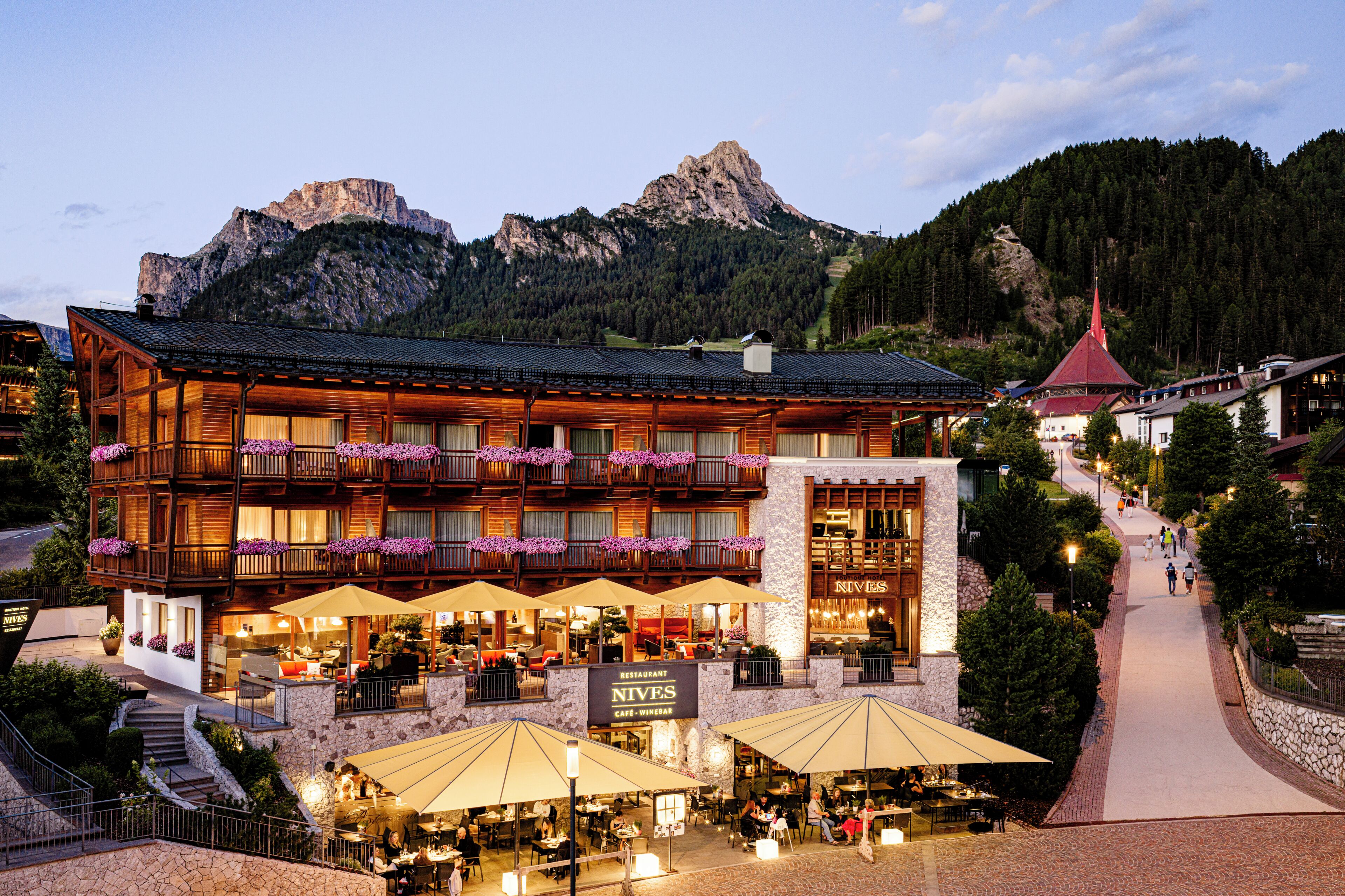 A hotel with a restaurant and cafe, outdoor seating with umbrellas, and a mountain backdrop.