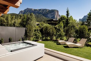 A hot tub with a view of a mountain range and a building in the background. - Boutique Hotel Nives (Selva di Val Gardena)