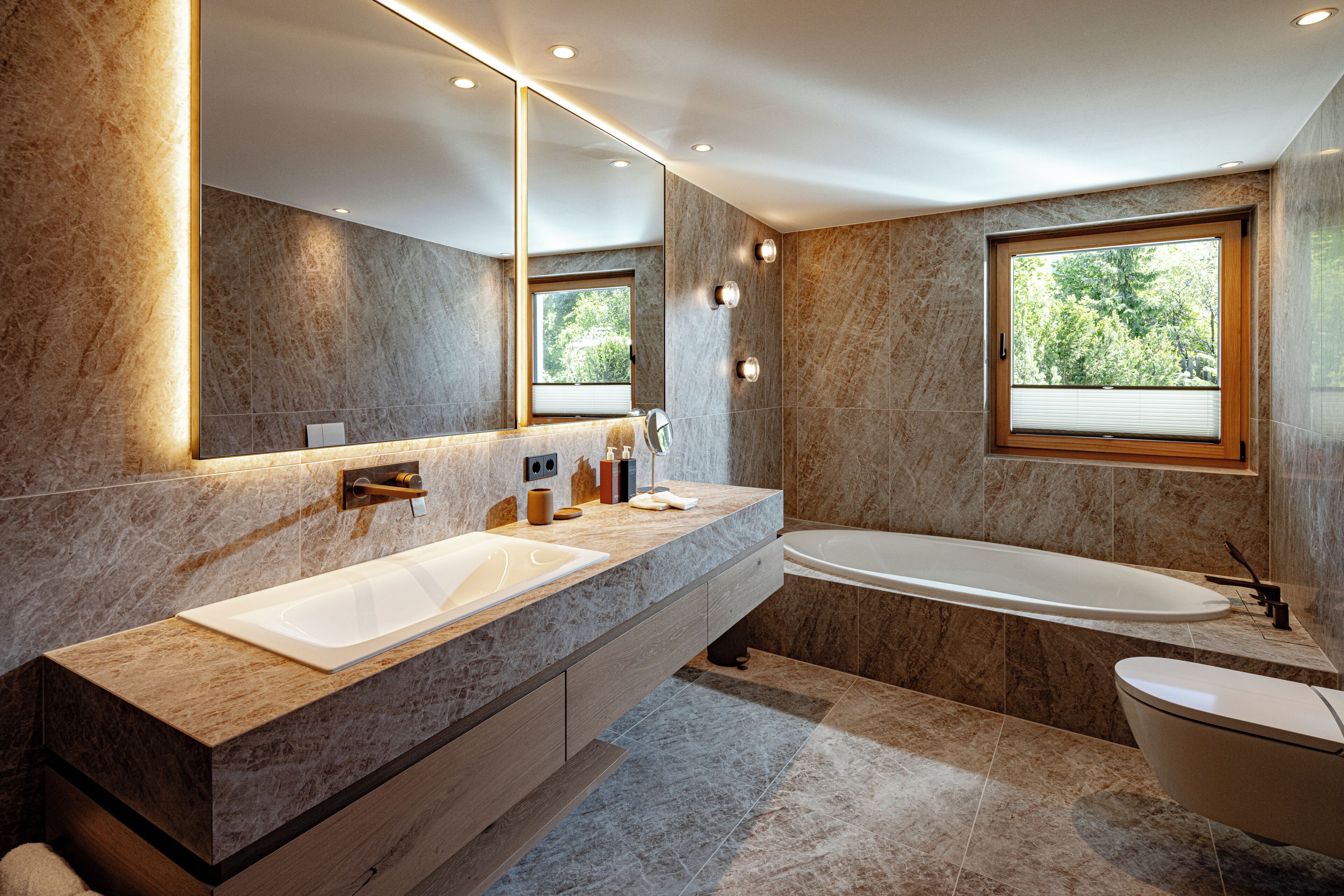 Un baño moderno con un espejo grande, dos lavamanos, una bañera y un ventanal que proporciona luz natural.