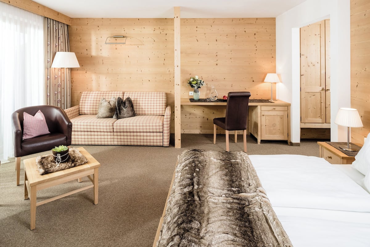 A hotel room with a bed, a desk, a sofa, a chair, and a small table.