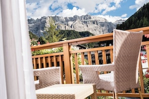 A balcony with wicker chairs and a wooden railing, overlooking a mountainous landscape with trees and a clear sky. - Boutique Hotel Nives (Selva di Val Gardena)
