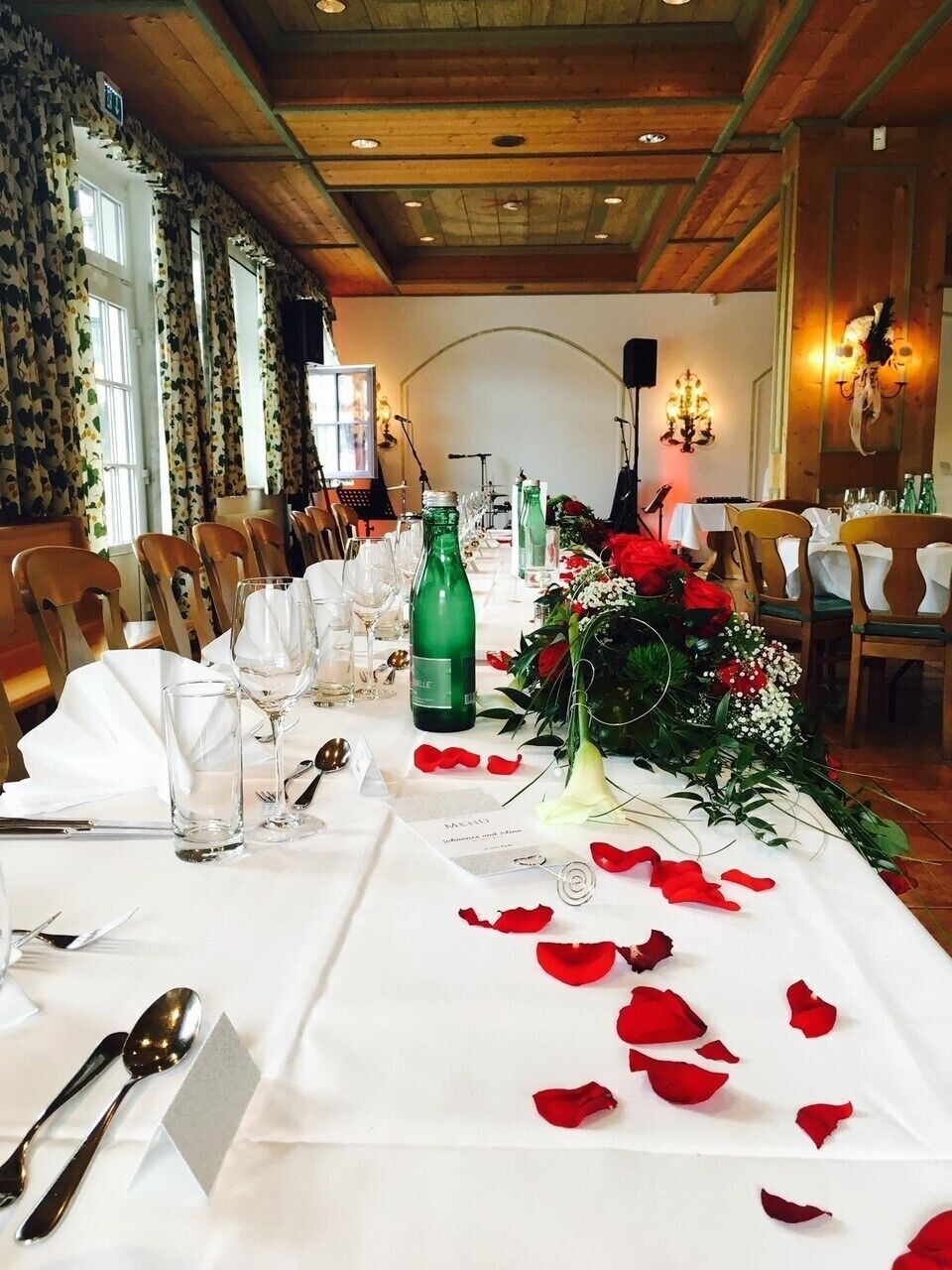 A banquet hall with long tables set for a formal event, featuring floral centerpieces and rose petals on the tablecloths.