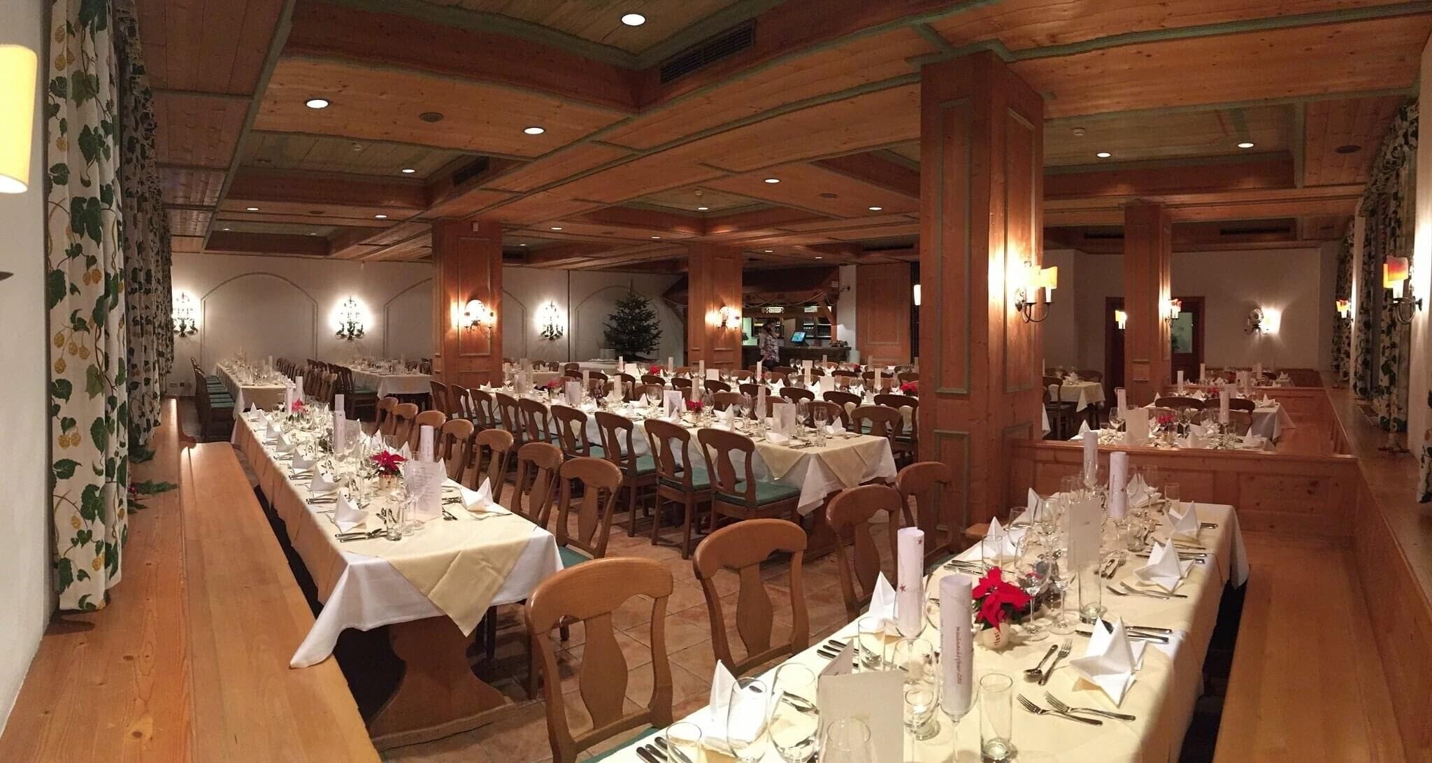 A large dining hall with multiple tables set for a meal, wooden paneling on the walls, and chandeliers.