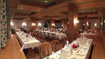 A large dining hall with multiple tables set for a meal, wooden paneling on the walls, and chandeliers.