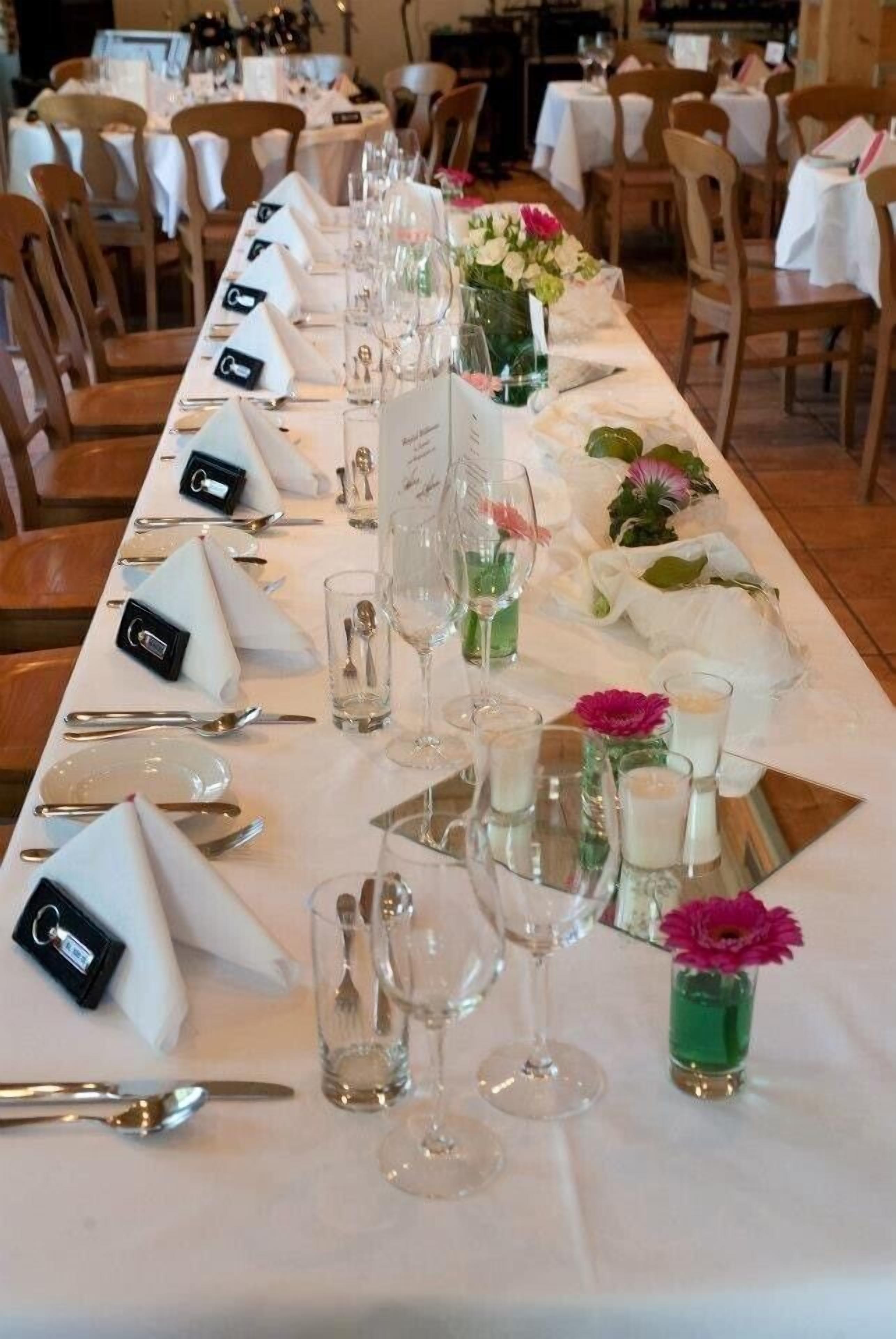Une longue table à manger, dressée avec de nombreuses assiettes, des verres et de petits vases ornés de fleurs.