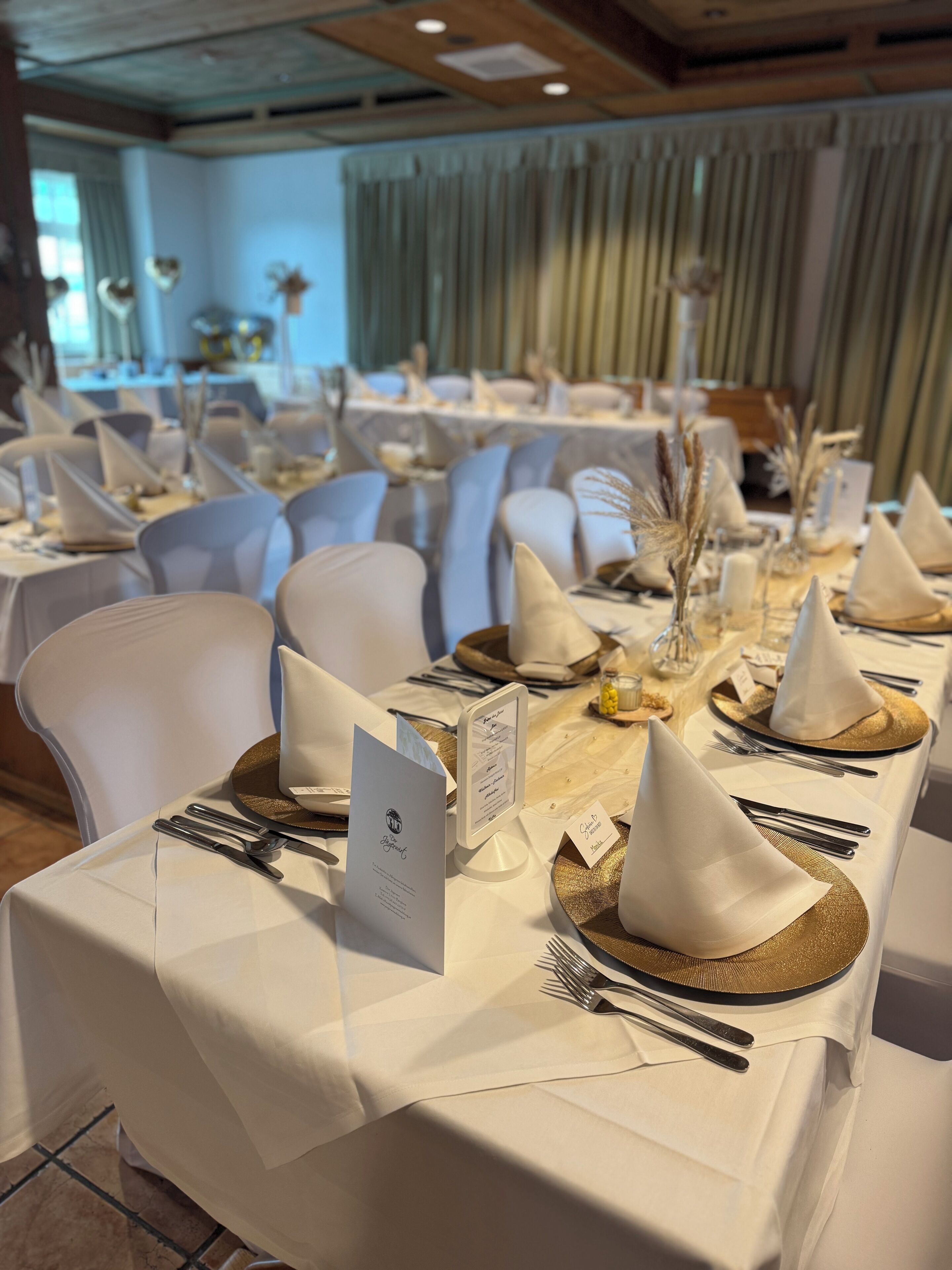 A banquet hall with tables set for a formal event, featuring white tablecloths, gold accents, and elegant table settings.