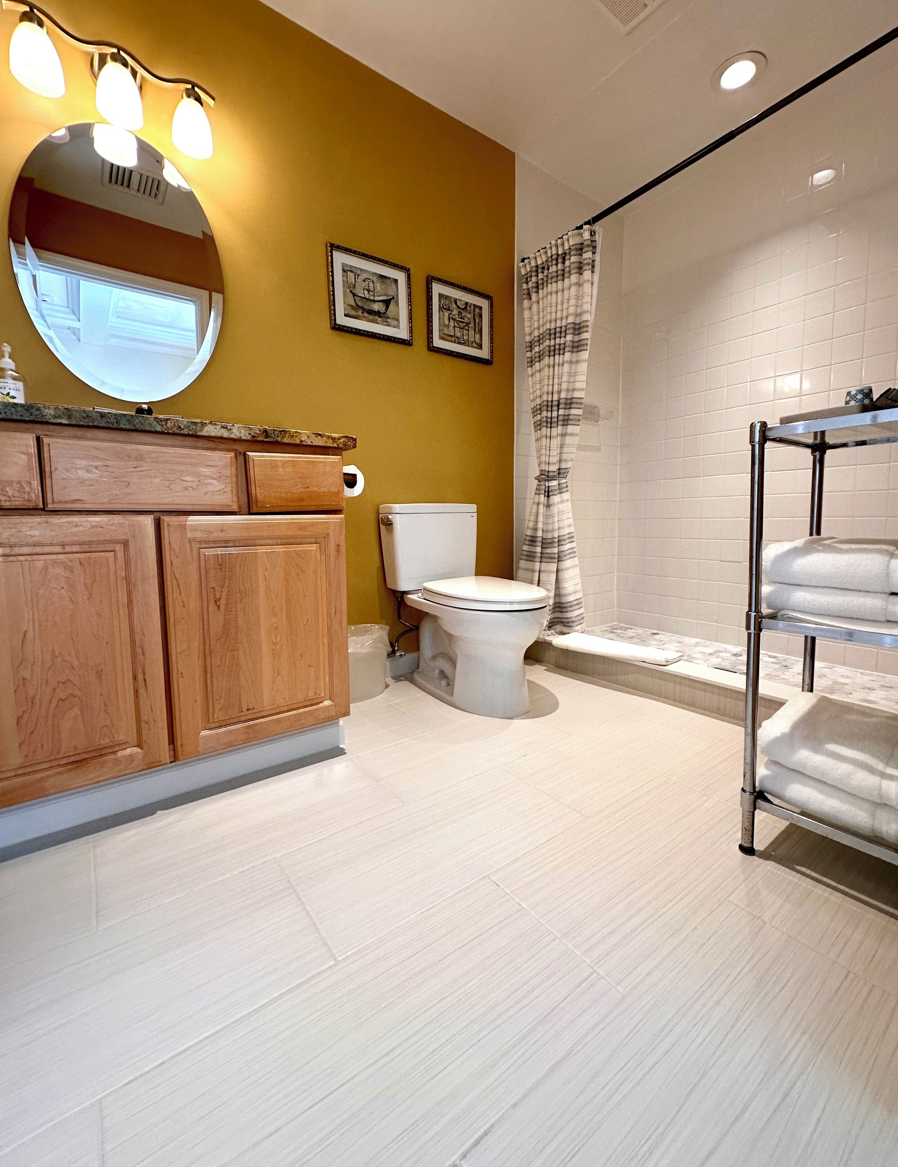 A bathroom with a wooden vanity, a toilet, a shower with a curtain, and a towel rack.