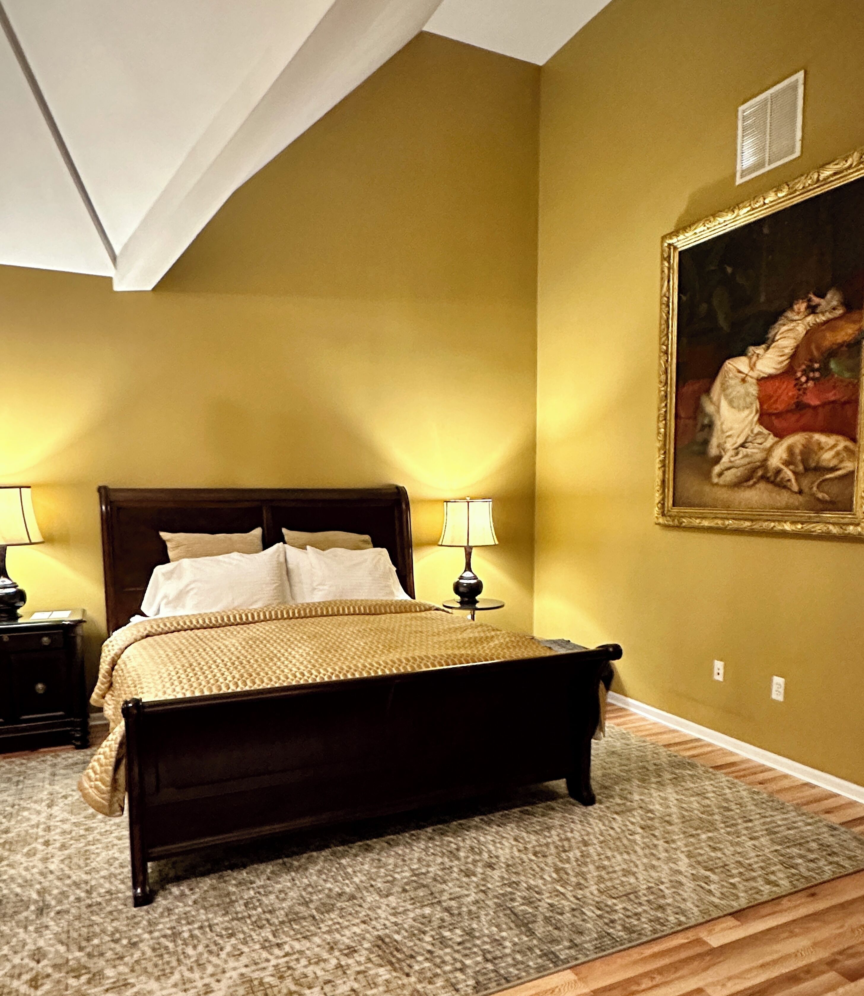 Un dormitorio con cama de madera, dos lámparas de noche, un cuadro en la pared y suelo alfombrado.