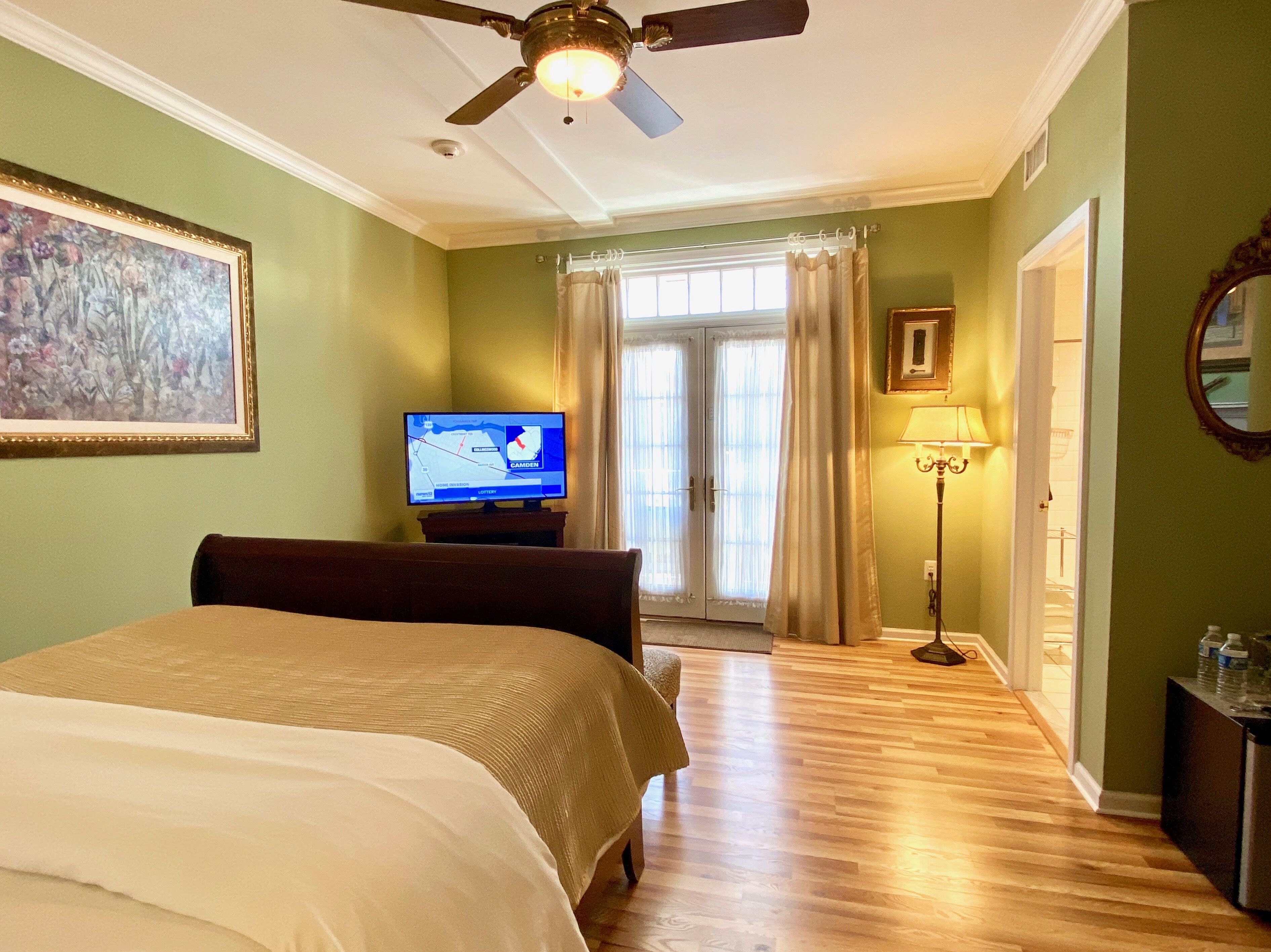 A hotel room with a bed, a television displaying a map, a ceiling fan, a lamp, and a door leading to a bathroom.