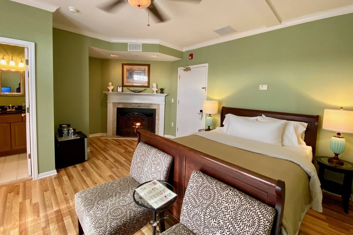 A hotel room with a bed, a fireplace, a seating area with a table, and a mirror.