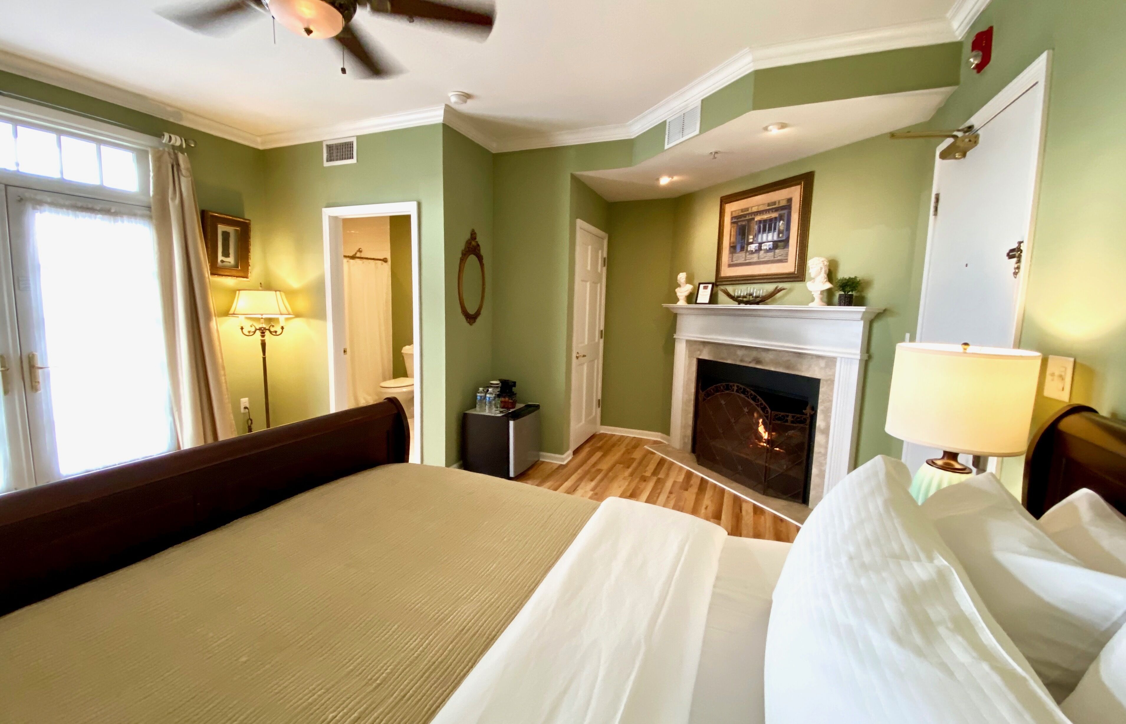 A bedroom with a bed, a fireplace, a ceiling fan, and a window with curtains.
