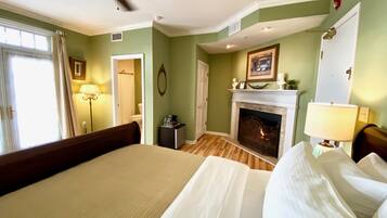 A bedroom with a bed, a fireplace, a ceiling fan, and a window with curtains.